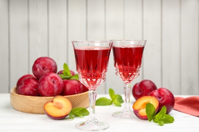 Delicious plum liquor, ripe fruits and mint on table against white background. Homemade strong alcoholic beverage