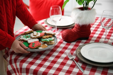 Woman with cookies setting table for Christmas dinner indoors, closeup
