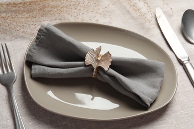 Photo of Plate with gray fabric napkin, decorative ring and cutlery on table