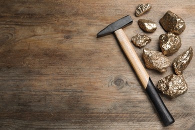 Pile of gold nuggets and hammer on wooden table, flat lay. Space for text