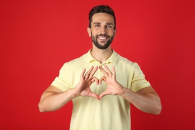 Happy man making heart with hands on red background