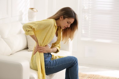 Photo of Woman suffering from back pain at home. Symptom of bad posture