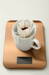 Cup with drip coffee bag and kitchen scales on white table