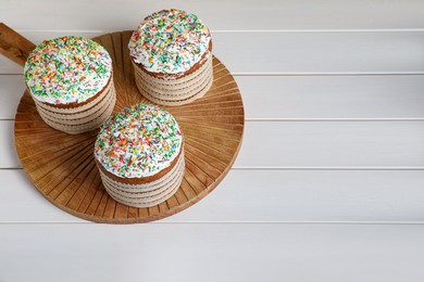 Photo of Traditional Easter cakes with sprinkles on white wooden table. Space for text