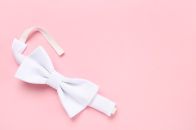 Stylish white bow tie on pink background, top view. Space for text
