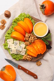 Photo of Delicious persimmon, blue cheese, nuts and honey served on white wooden table, flat lay