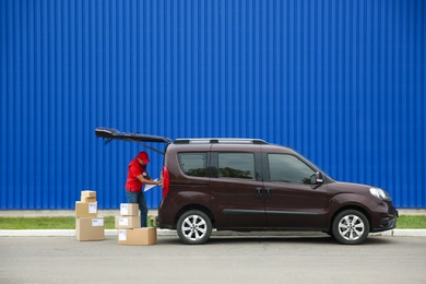 Courier loading packages in car outdoors, space for text