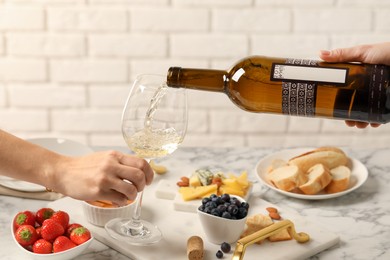 Woman pouring wine from bottle into glass over table with different snacks, closeup
