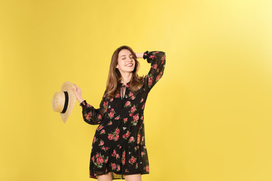 Young woman wearing floral print dress with straw hat on yellow background