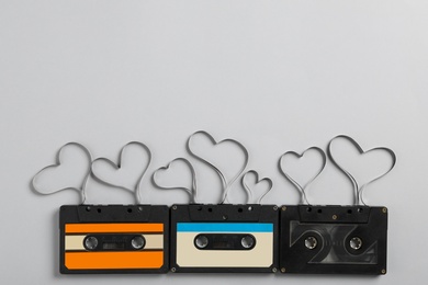 Music cassettes and hearts made of tape on light grey background, flat lay with space for text. Listening love songs