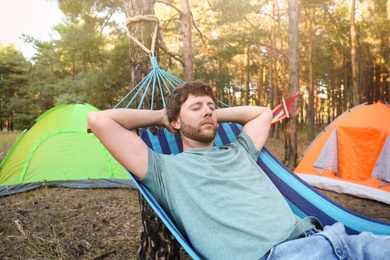 Photo of Man sleeping in comfortable hammock near tents outdoors