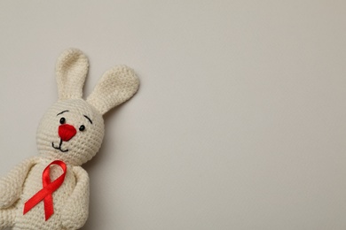 Cute knitted toy bunny with red ribbon on beige background, top view and space for text. AIDS disease awareness