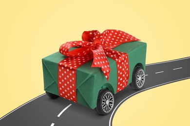 Image of Gift box with wheels riding on asphalt road against pale yellow background. Delivery service
