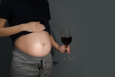 Pregnant woman with glass of red wine on dark background, space for text. Alcohol addiction