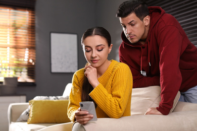 Distrustful man peering into girlfriend's smartphone at home. Jealousy in relationship