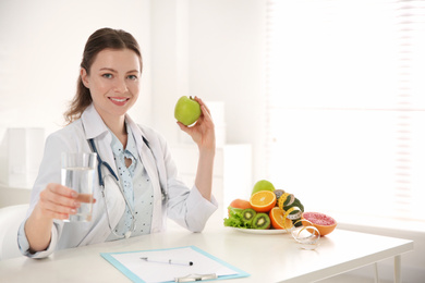 Nutritionist with glass of water and apple at desk in office. Space for text