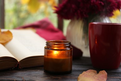 Photo of Burning scented candle, cup of tea and book on wooden table. Autumn atmosphere