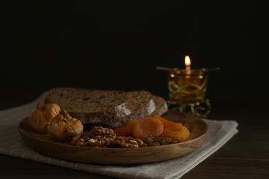 Bread, dried fruits, walnuts and burning candle on wooden table. Great Lent season