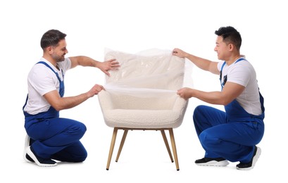 Photo of Workers covering armchair with plastic film on white background