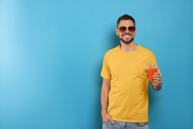 Man holding glass of delicious juice on light blue background, space for text