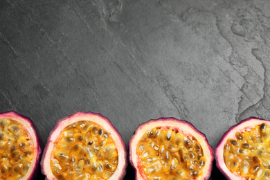 Halves of passion fruits (maracuyas) on black slate table, flat lay. Space for text