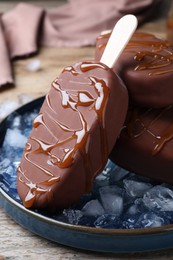 Photo of Delicious glazed ice cream bars and ice cubes on wooden table, closeup