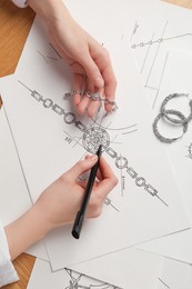 Photo of Jeweler drawing sketch of elegant bracelet on paper at wooden table, top view