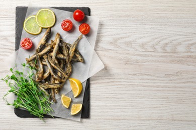 Photo of Slate board with delicious fried anchovies, lime and tomatoes on white wooden table, top view. Space for text