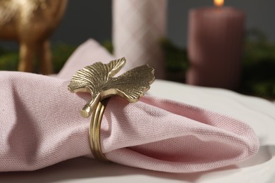 Pink fabric napkin with beautiful decorative ring for table setting on plate, closeup