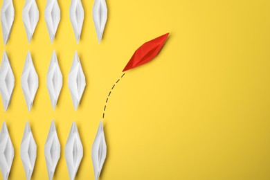 Photo of Red paper boat floating away from others on yellow background, flat lay with space for text. Uniqueness concept