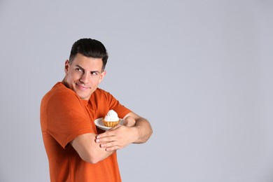 Photo of Greedy man hiding cupcake on grey background, space for text