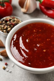 Spicy chili sauce in bowl on grey table, closeup