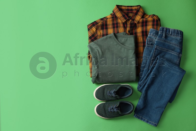 Stylish child clothes and shoes on green background, flat lay. Space for text