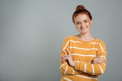 Candid portrait of happy red haired woman with charming smile on grey background, space for text