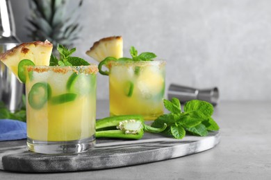 Photo of Glasses of spicy pineapple cocktail with jalapeno and mint on grey table. Space for text