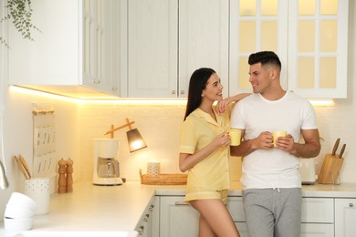 Photo of Happy couple wearing pyjamas with cups of coffee in kitchen