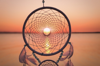 Beautiful handmade dream catcher near river at sunset