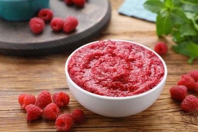 Raspberry puree in bowl and fresh berries on wooden table, closeup