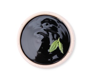 Photo of Balsamic glaze with basil leaves in bowl isolated on white, top view