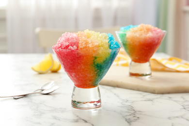Rainbow shaving ice in glass dessert bowls on white marble table indoors, closeup