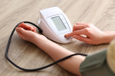 Woman checking blood pressure at wooden table indoors, closeup
