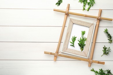 Flat lay composition with bamboo frame and green leaves on white wooden table. Space for text