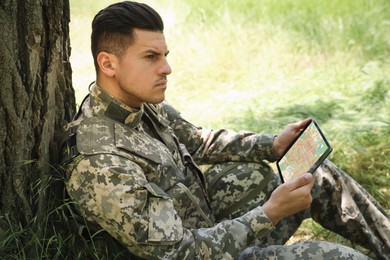 Soldier using tablet near tree in forest