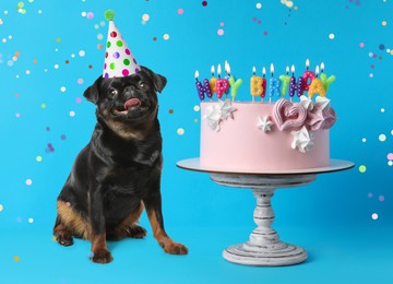 Cute dog with party hat and delicious birthday cake on blue background