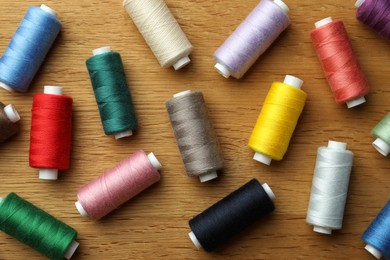 Many colorful sewing threads on wooden table, flat lay