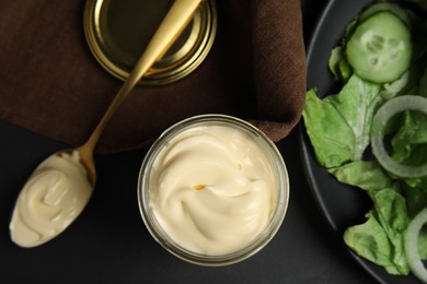 Photo of Jar and spoon with delicious mayonnaise near fresh salad on black table, flat lay