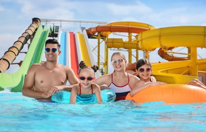 Happy family with inflatable rings in swimming pool at water park