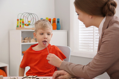 Speech therapist using logopedic probe during session with little boy in office