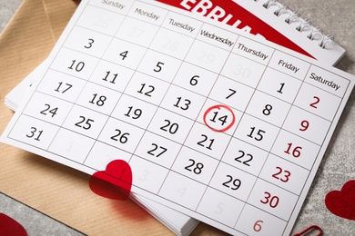 Calendar with marked Valentine's Day, envelope and hearts on grey table