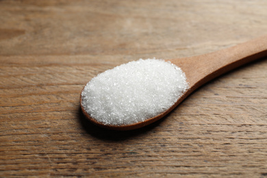 Photo of Spoon of white sugar on wooden table, closeup